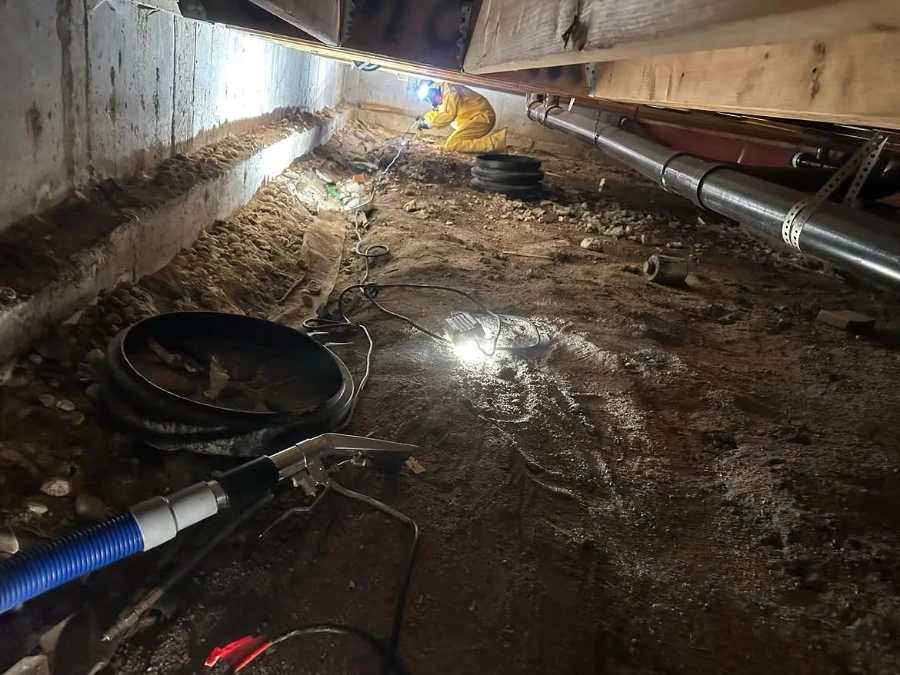 Technician performing crawlspace water extraction and drainage repair under a Minneapolis home